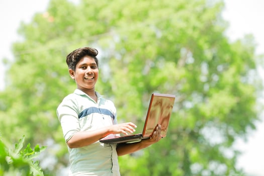 Indian boy studying in farm, holding laptop in hand , poor indian kids photo