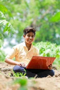 Indian boy studying in farm, holding laptop in hand , poor indian kids photo