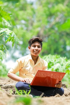 Indian boy studying in farm, holding laptop in hand , poor indian kids photo