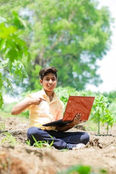 Indian boy studying in farm, holding laptop in hand , poor indian kids photo