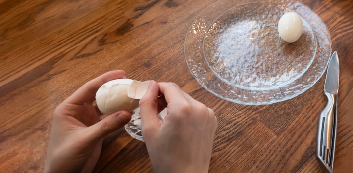Woman peeling boiled egg on wooden background photo