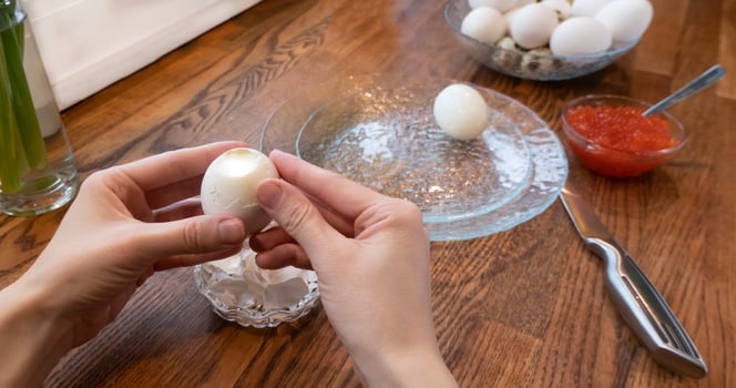 Woman peeling boiled egg on wooden background photo