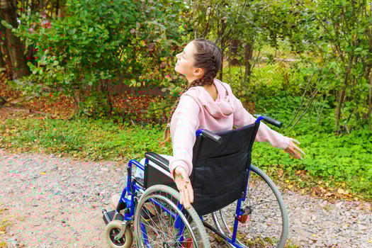 Young happy handicap woman in wheelchair on road in hospital park enjoying freedom. Paralyzed girl in invalid chair for disabled people outdoor in nature. Rehabilitation concept. photo