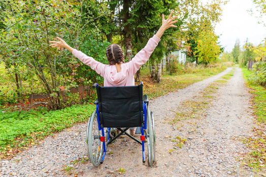 Young happy handicap woman in wheelchair on road in hospital park enjoying freedom. Paralyzed girl in invalid chair for disabled people outdoor in nature. Rehabilitation concept. photo