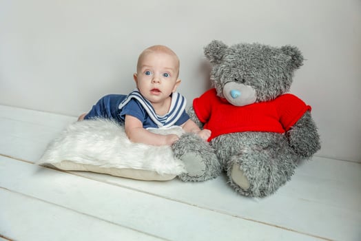 Infant baby boy lies on pillow with teddy bear toy on white bedroom background photo