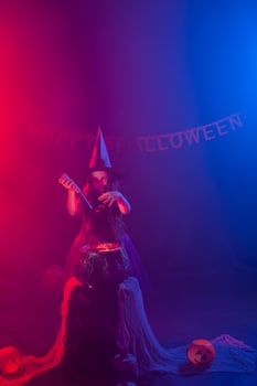 Child girl witch preparing a potion in the cauldron at halloween holidays. photo