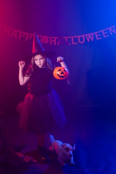 Funny child girl in witch costume for Halloween with pumpkin Jack and dog. photo