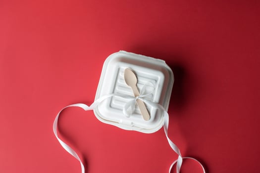 Gift box for a small bento cake with a wooden spoon, closed on a yellow background. White ribbon bow photo