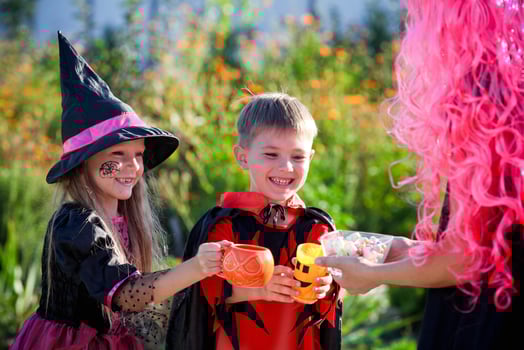 children trick or treat in Halloween costume . A little boys and a girl in suits  receive  candy from a woman dressed  in a pink wig . photo