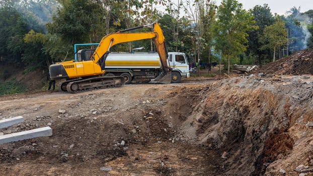 A view of a yellow backhoe and a white water truck stacked on a mound. photo