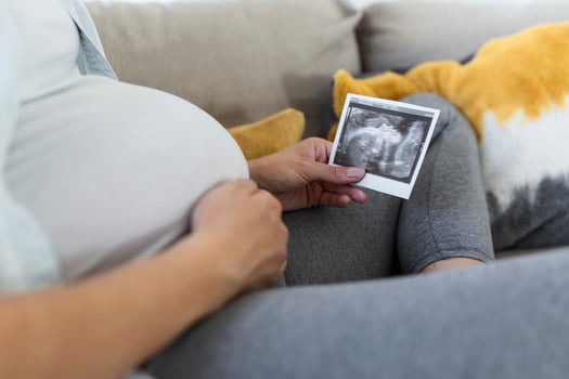 Pregnant woman holding ultrasound image. Concept of pregnancy, health care, gynecology, medicine. Young mother waiting of the baby. Close-up, copy space, indoors. photo