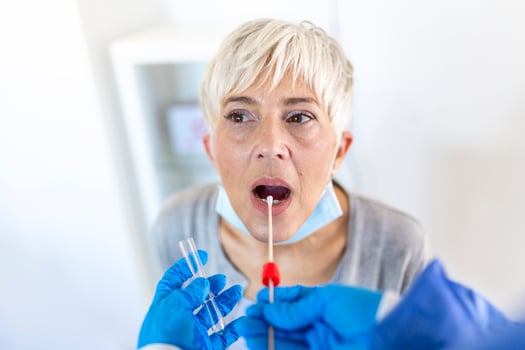 mature Caucasian woman in a clinical setting being swabbed by a healthcare worker in protective garb to determine if she has contracted the coronavirus or COVID-19. photo