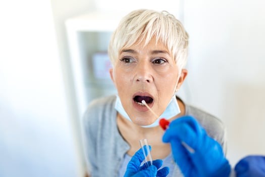 mature Caucasian woman in a clinical setting being swabbed by a healthcare worker in protective garb to determine if she has contracted the coronavirus or COVID-19. photo