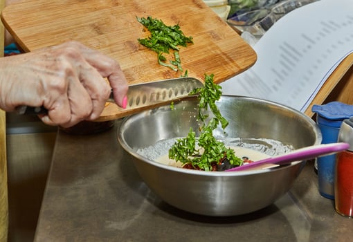 Chef throws basil leaves on wooden cutting board with knife into dish photo