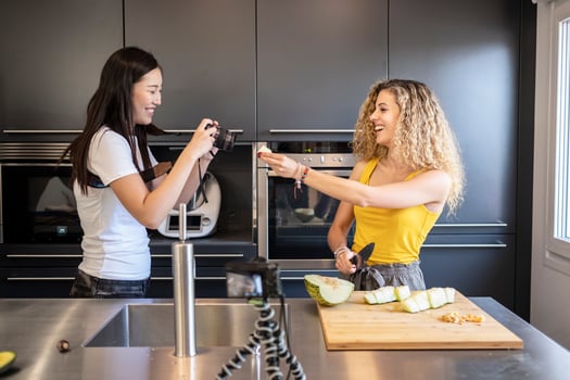asiatic woman filming caucasian woman cutting fruit in a kitchen. photo