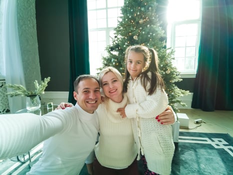 family, holidays, technology and people - smiling mother, father and little girl making selfie with camera over living room and christmas tree background photo
