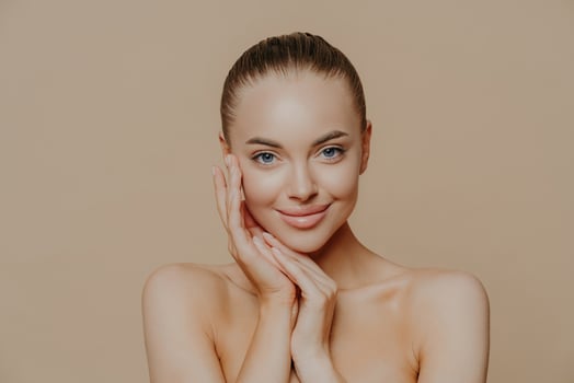 Natural beauty portrait. Fresh skin, gentle smile. Naked pose against beige background. Face touch, minimal makeup. photo