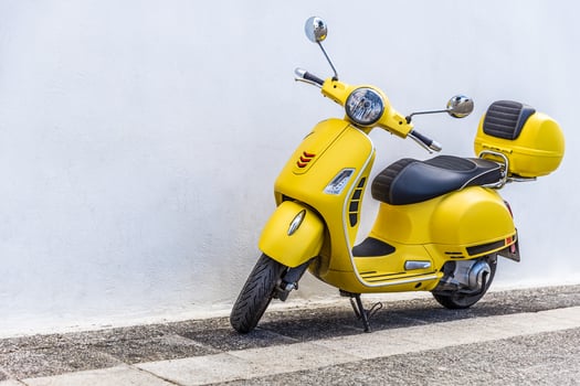 A yellow scooter parked against a wall photo