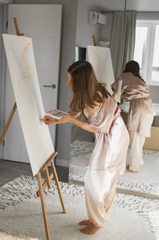 Young woman artist painting on canvas on the easel at home in bedroom - art and creativity concept photo