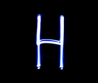 H Hotel alphabet hand writing blue light  over black background. photo