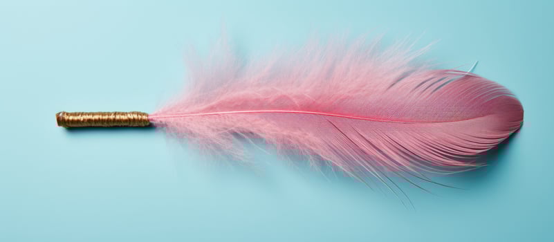 Photo of a vibrant pink feather with a shimmering gold tip against a captivating blue backdrop with copy space