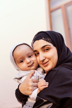 Young Muslim woman in hijab holding her 1-year-old baby boy, hugging and kissing. Happy Muslim mother in abaya clothing kiss and play with her little child photo