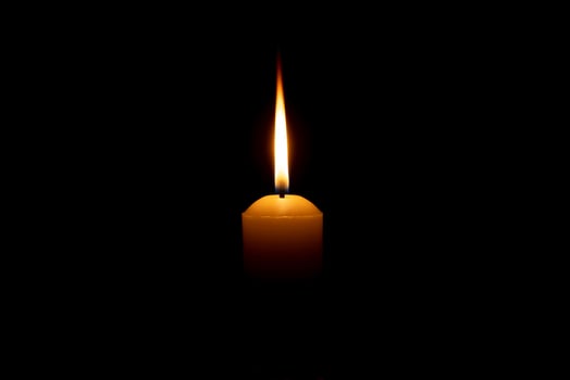 Single burning candle flame or light glowing on a big white candle on black or dark background on table in church for Christmas, funeral or memorial service with copy space. photo