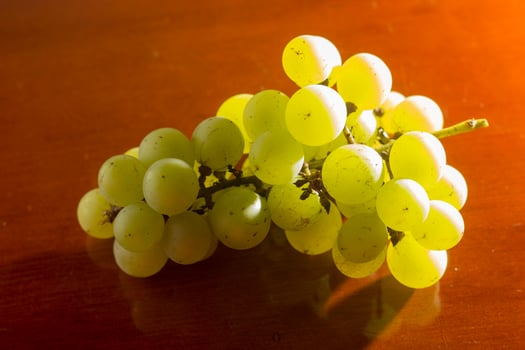 bunch of green grapes on wooden plinth isolated light from behind, orange background. negative space photo