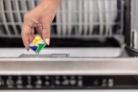 Detail of a female hand putting colorful detergent tablet into the dishwasher photo