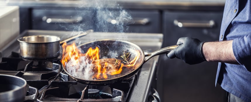 Chef in the kitchen leans pan to the side for alcohol in it to catch fire for gas stove, starting to flambe the food photo