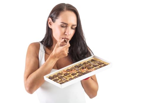 Attractive dark-haired woman is eating a chocolate candy while holding a full candy box. Closed eyes show how tasty the chocolate is. Isolated background photo