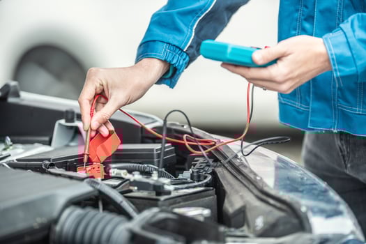 Car electrician or mechanic checks voltage in car battery inside the car engine with open hood photo