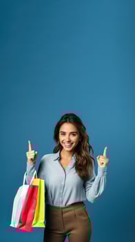 Smiling young brunette woman holding shopping bags with purchases after shopping point finger aside isolated on blue background photo