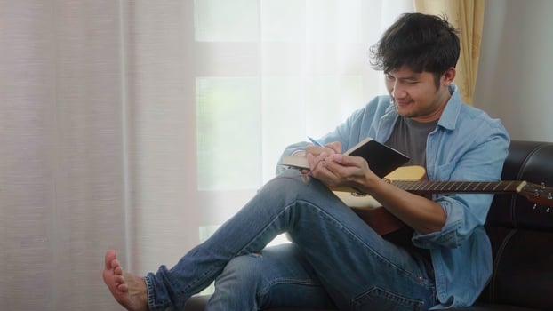 Asian man Songwriter writing ideas on notebook with acoustic guitar in home. photo