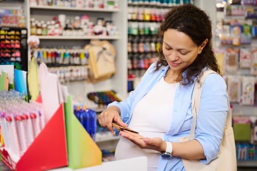 Pleasant pregnant woman shopping for school supplies in school stationery store, choosing color pencils. Drawing. Art photo