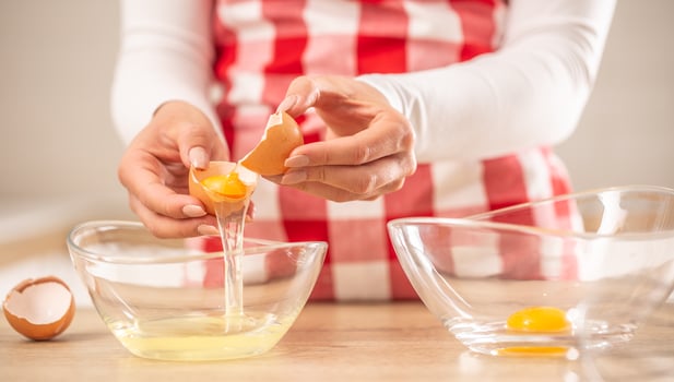 Detail of woman's hands separating egg yolks from the whites into two glass bowls photo