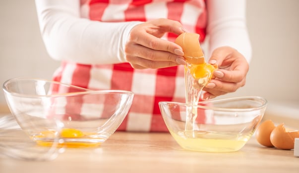 Detail of woman's hands separating egg yolks from the whites into two glass bowls photo