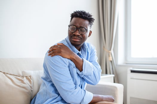 Pain in his shoulder. Upper arm pain, People with body-muscles problem, Healthcare And Medicine concept. Attractive young man sitting on the sofa and holding painful shoulder with another hand. photo