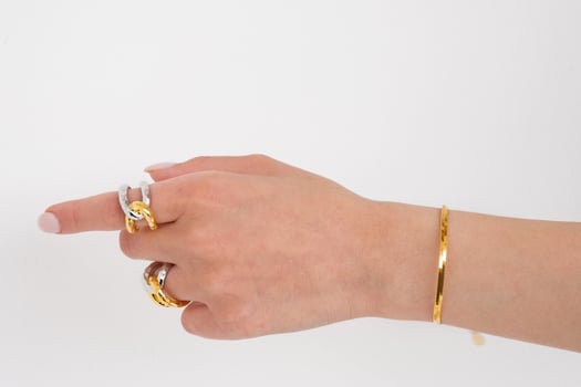 Woman hand wearing golden Snake Chain bracelet and Interlocked Golden and Silver Rings set against a white background. Beautiful valentine's gift. photo