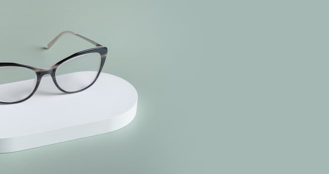 Podium with eyeglasses on pastel green background. Optical store, vision test, stylish glasses concept. photo