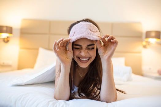 Beautiful girl in bed with sleeping eye mask relaxing. beautiful excited woman in sleeping eye mask lying in bed photo