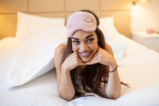 Beautiful girl in bed with sleeping eye mask relaxing. beautiful excited woman in sleeping eye mask lying in bed photo