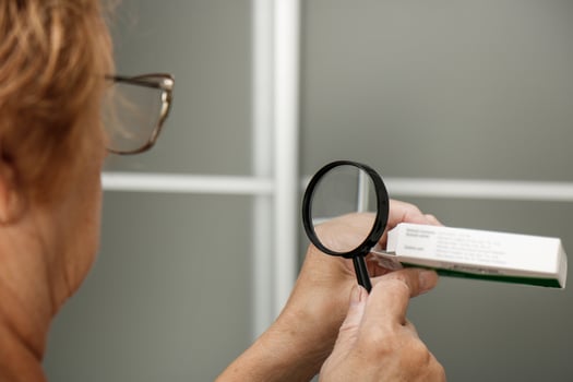 an elderly woman carefully examines a package of medicines through a magnifying glass photo