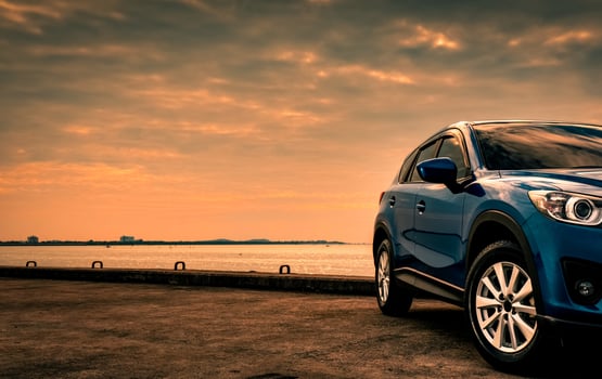 Blue compact SUV car with sport and modern design parked on concrete road by the sea at sunset in the evening. Hybrid and electric car technology concept. Car parking space. Automotive industry. photo