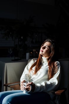 Woman in warm white winter sweater sitting at windowsill at home at christmas eve holding cup with marshmallows photo