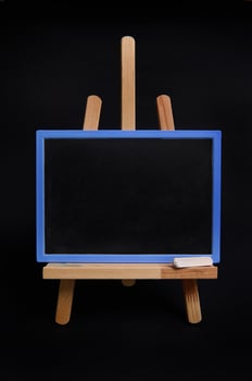 Close-up of a chalk board with empty space for text, standing on a wooden table easel isolated on black background with copy space. photo