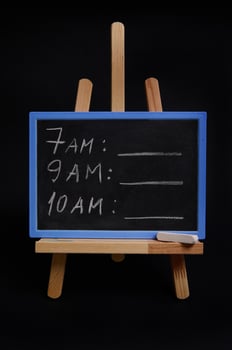 Lettering schedule with a white chalk, on a blackboard standing on a wooden table easel, isolated over black background with copy space. Planning concepts, time management, timetable and timing. photo