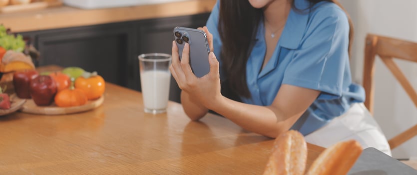 A young woman with a beautiful face in a blue shirt with long hair eating fruit sitting inside the kitchen at home with a laptop and notebook for relaxation, Concept Vacation. photo