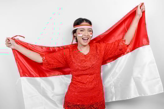 Happy smiling Indonesian woman wearing red kebaya and headband holding Indonesia's flag to celebrate Indonesia Independence Day isolated over white background. photo