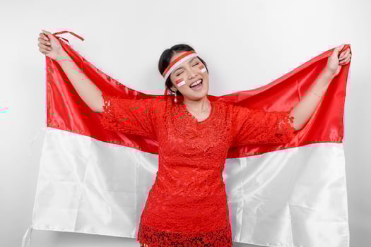 Happy smiling Indonesian woman wearing red kebaya and headband holding Indonesia's flag to celebrate Indonesia Independence Day isolated over white background. photo